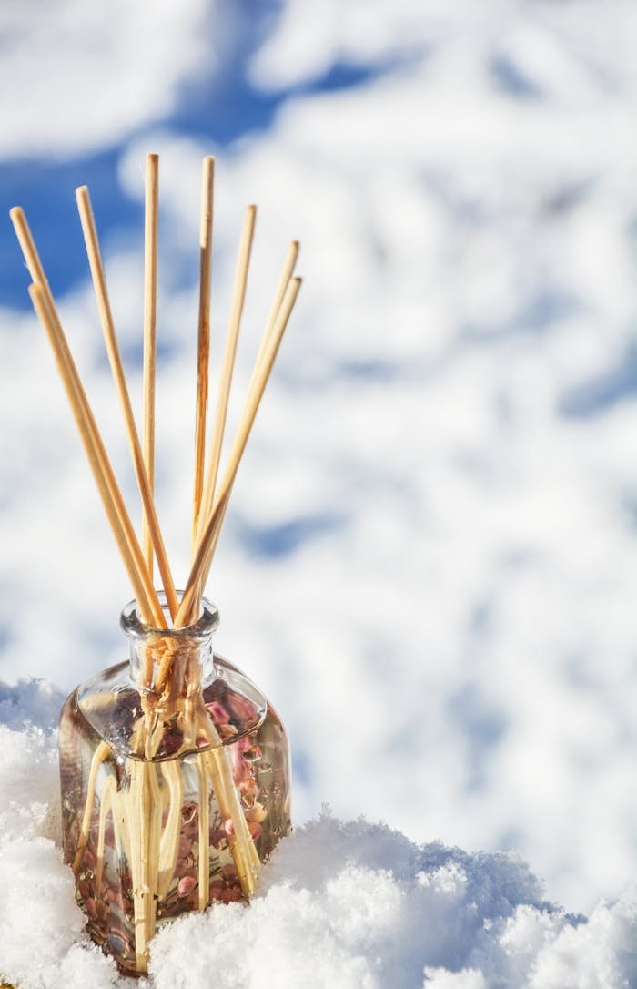 A fragrant glass diffuser bottle with sticks in the snow, emitting an aromatic scent.