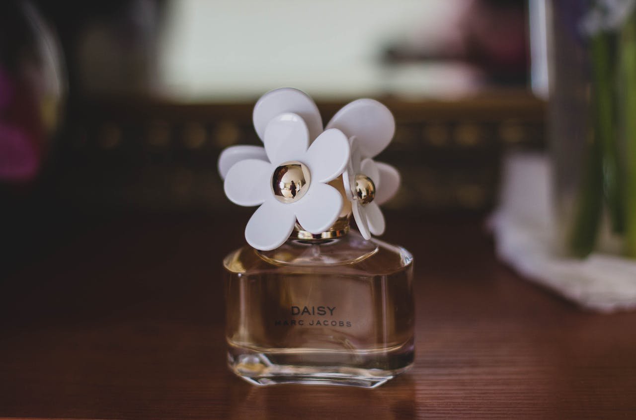 Close-up of a Marc Jacobs Daisy perfume bottle with flower caps on a wooden table.