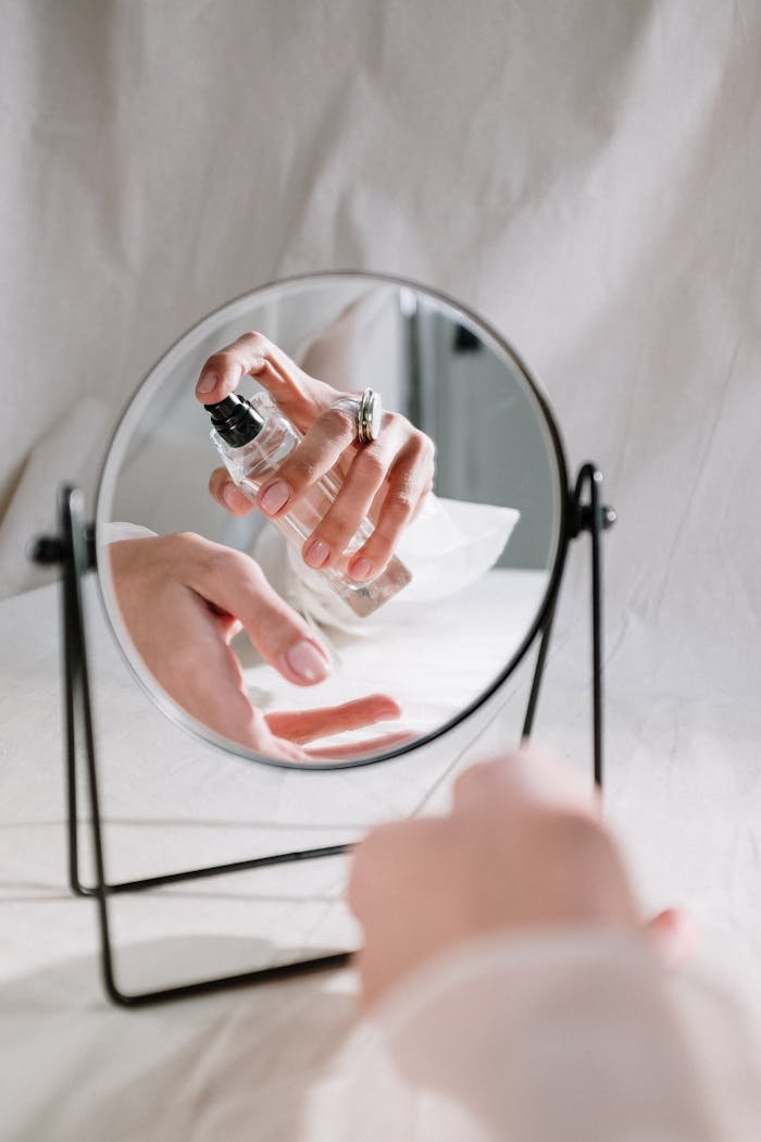 A graceful hand holding a perfume bottle reflected in a mirror, creating an elegant scene.