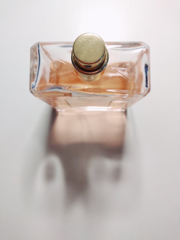 A close-up shot of an elegant perfume bottle with a golden cap on a white surface casting a shadow.