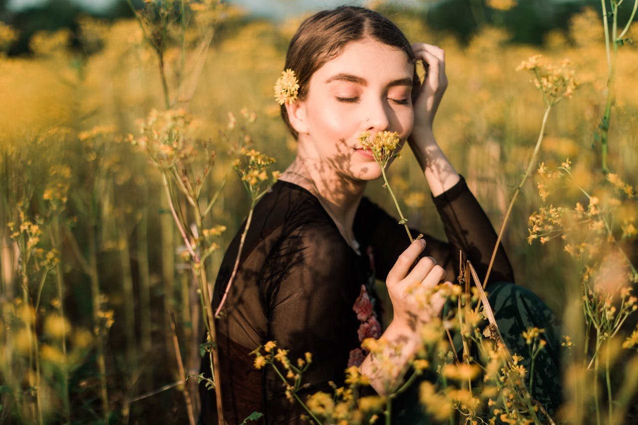 Woman enjoying the fragrance of yellow flowers in a sunlit field.