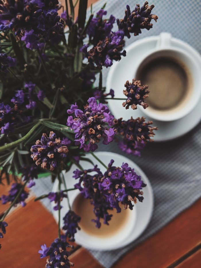 A top-down view of lavender flowers next to coffee cups on a wooden table, creating a cozy ambiance.