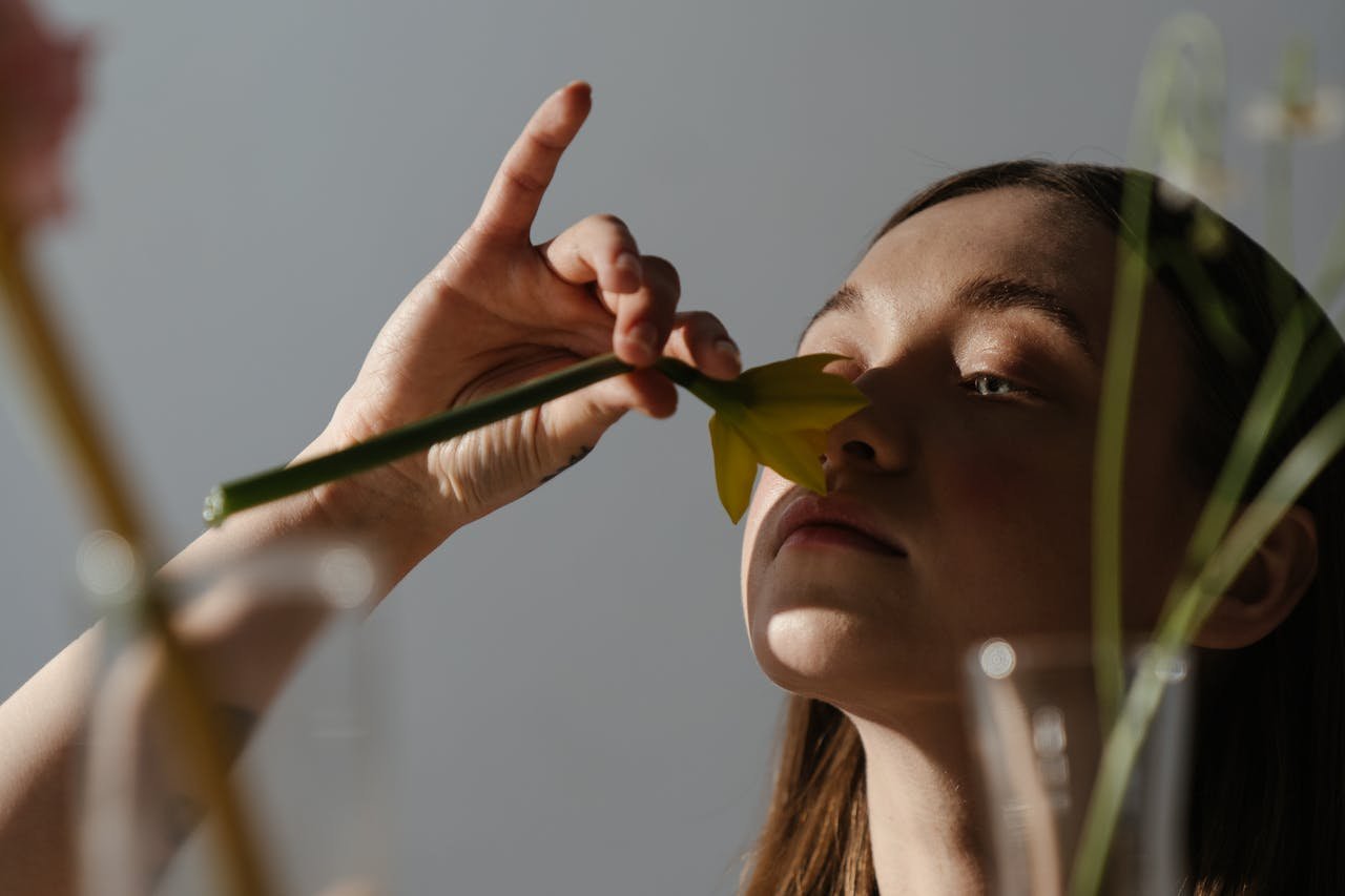 Adult woman gently smelling a daffodil flower indoors, captured in warm natural light.